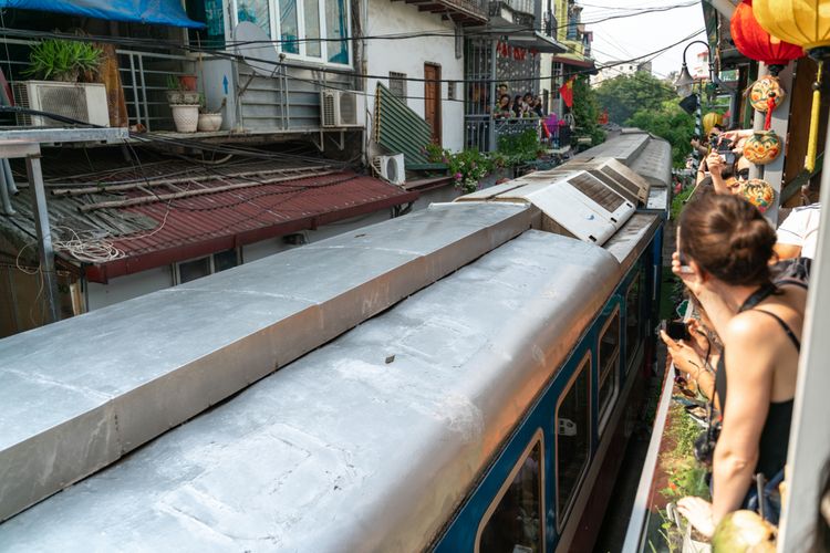 Para turis menyaksikan kereta lewat dari pinggir kafe rel kereta di Hanoi, Vietnam.