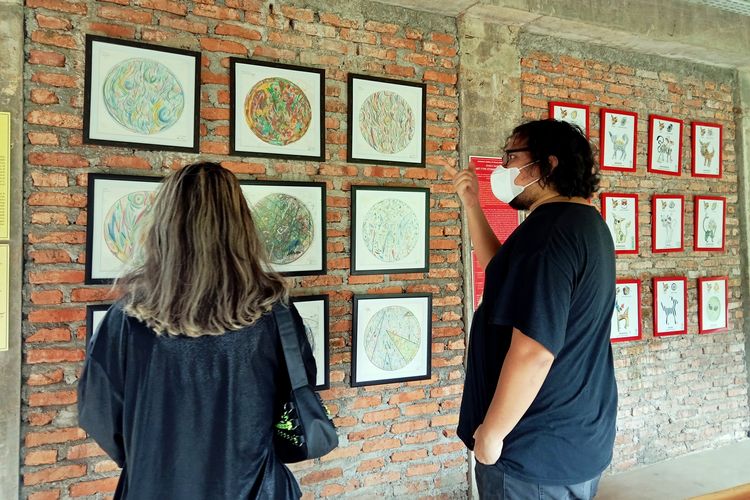 Andra Semesta, seniman sekaligus pengelola Semesta's Gallery saat menjelaskan lukisan yang dipajang kepada pengunjung. 