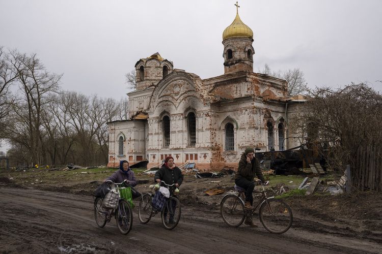 Warga berjalan dengan sepeda mereka di depan sebuah gereja yang rusak, di Lukashivka, di utara Ukraina, Jumat, 22 April 2022.