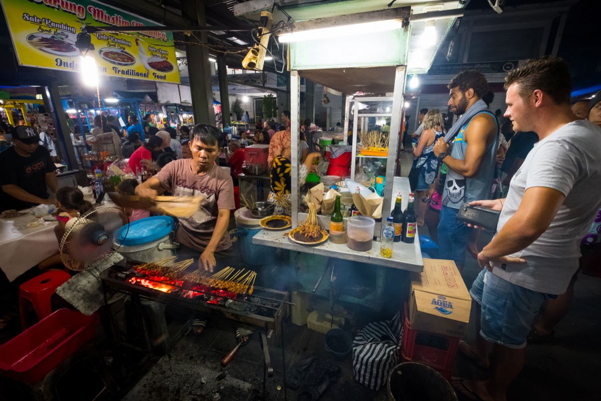 Ilustrasi wisatawan asing tengah makan di kedai sate. 