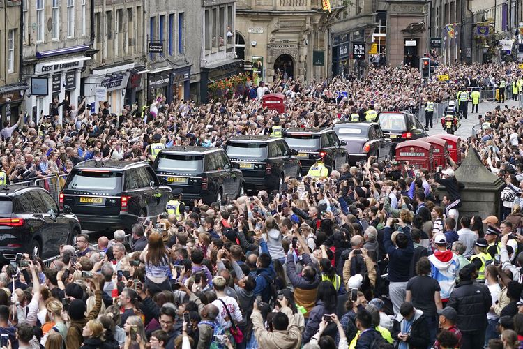 Massa menyaksikan mobil jenazah yang membawa peti mati Ratu Elizabeth II, yang dibungkus dengan Royal Standard of Scotland, melewati Mercat Cross di Edinburgh, Minggu (11/9/2022) saat melanjutkan perjalanannya ke Istana Holyroodhouse dari Balmoral.