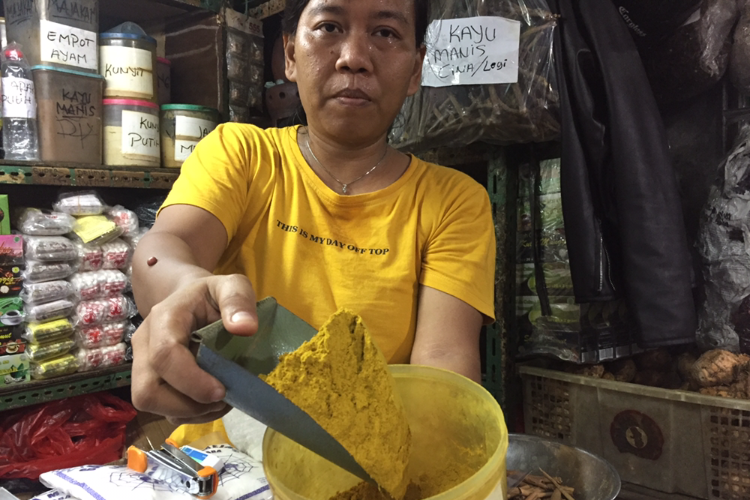 Ia, pedagang jamu di Pasar Jatinegara sedang membawa bubuk kunyit salah satu dagangannya. 