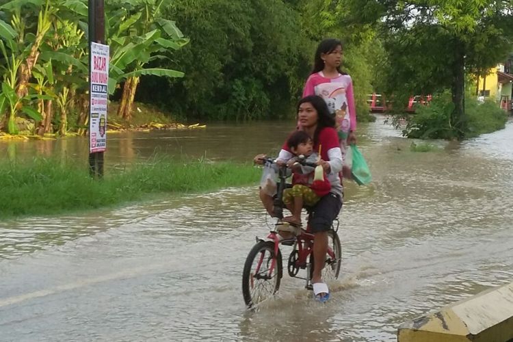 Anak-anak memakai sepeda menerjang banjir di Jalan Kebundalem, Kendal.