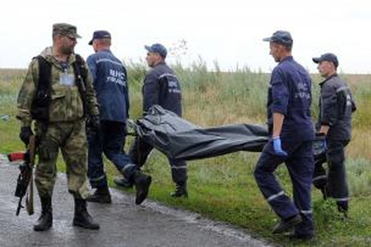 Petugas penolong Ukraina melewati seorang anggota kelompok separatis pro-Rusia ketika mengangkut jenazah penumpang Malaysia Airlines MH17 di Grabovo, Sabtu (19/7/2014).