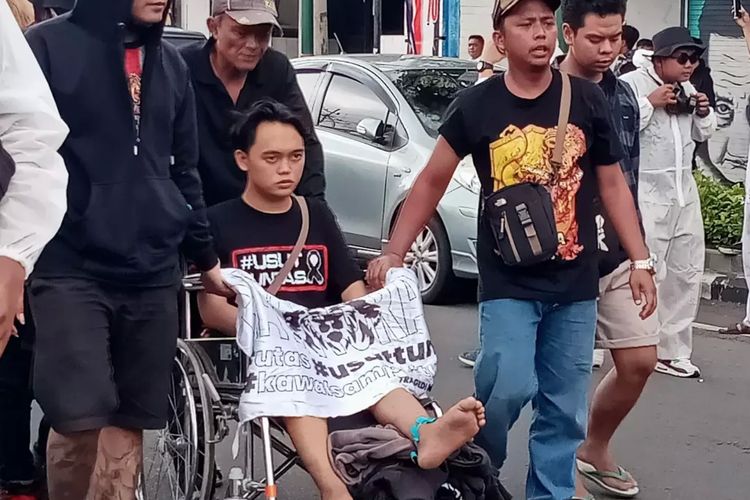 Salah satu massa aksi damai asal Aremania Sidoarjo, Muhammad Anugrah Bustom menggunakan kursi roda dibantu dengan Aremania lainnya pada Kamis (10/11/2022). 