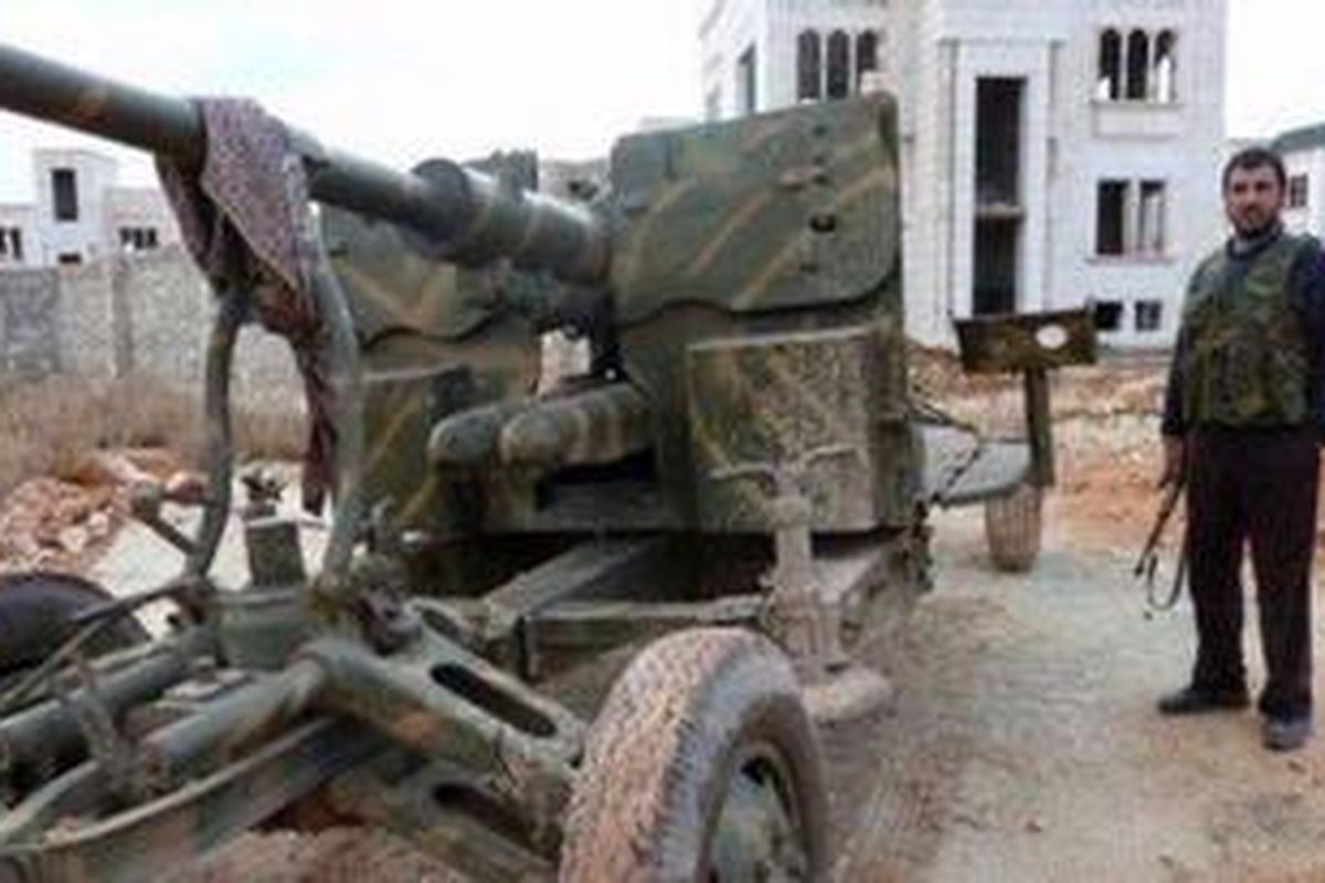 Seorang pejuang Front Al-Nusra berdiri di dekat sebuah meriam di pangkalan militer Sheikh Suleiman, 25 kilometer sebelah utara kota Aleppo, Suriah. Front Al-Nusra berhasil merebut pangkalan militer strategis ini dari tangan pasukan pemerintah.