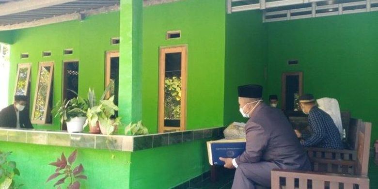 Prosesi akad nikah Sugiyanto dan Ngatini pada Minggu (18/7/2021). Karena pengantin pria terkonfirmasi positif Covid-19 maka posisinya berjarak di dalam teras dan Penghulu di luar teras. 
