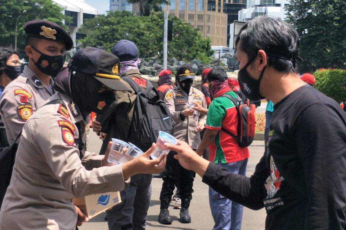 Sejumlah polisi membagikan air minum kepada para buruh yang menggelar aksi demonstrasi di depan di sekitar Bundaran Patung Kuda Arjuna Wijaya, Senin (12/4/2021).