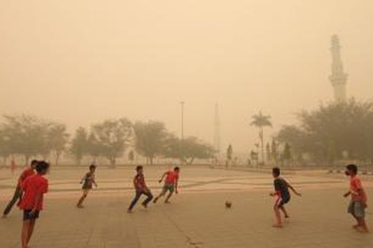 Sejumlah anak bermain bola di area Masjid Agung An Nur, Pekanbaru, yang diselimuti kabut asap, Kamis (13/3/2014). Kabut asap yang disebabkan kebakaran lahan dan hutan tersebut semakin pekat. Pemerintah Provinsi Riau mengimbau warga untuk menggunakan masker terkait kualitas udara yang memburuk. 