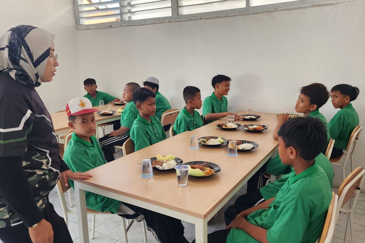 Para siswa SRMP 28 Pasuruan sedang menikmati menu makan siang dengan menu lengkap mulai dari ikan, buah, jus buah dan sayur, Selasa (14/10/2025). 