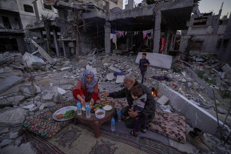 Keluarga Al-Naji dari Palestina bersiap untuk berbuka puasa pada hari pertama bulan suci Ramadan sambil duduk di tengah reruntuhan rumah keluarga mereka di Deir el-Balah, Jalur Gaza tengah, pada 11 Maret 2024, di tengah pertempuran yang sedang berlangsung antara Israel dan kelompok militan Hamas. 
