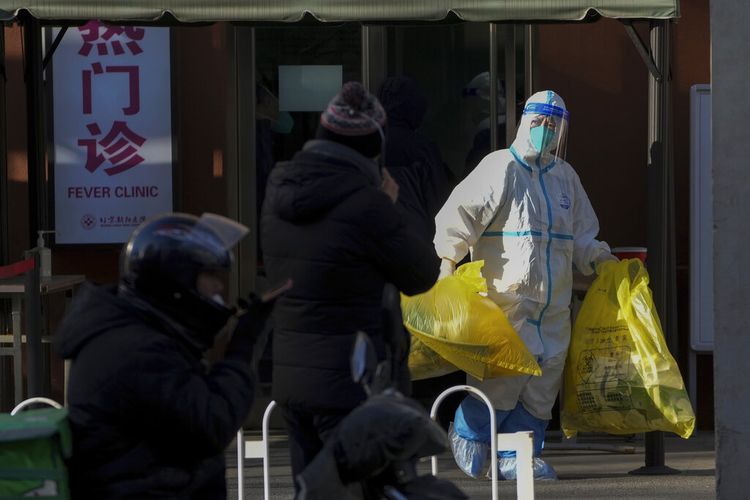 Seorang pekerja medis mengenakan pakaian pelindung membawa kantong kuning berisi limbah medis dari klinik demam di Beijing, Senin, 19 Desember 2022. Otoritas kesehatan China pada Senin mengumumkan dua kematian tambahan akibat Covid-19.