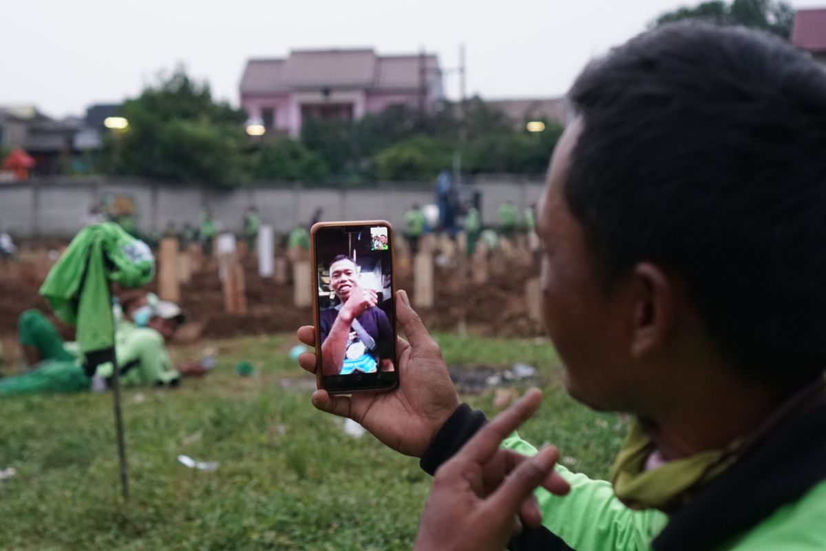 Para penggali kubur melakukan panggilan video sembari menunggu peti jenazah pasien Covid-19 datang di Taman Pemakaman Umum (TPU) Srengseng Sawah, Jagakarsa, Jakarta Selatan pada Jumat (15/1/2021). TPU Srengseng Sawah dijadikan sebagai tempat pemakaman jenazah pasien Covid-19 sejak Selasa (12/1/2021). TPU Srengseng Sawah memiliki lahan seluas 0,5 hektar dan bisa menampung sekitar 700 makam untuk jenazah pasien Covid-19.