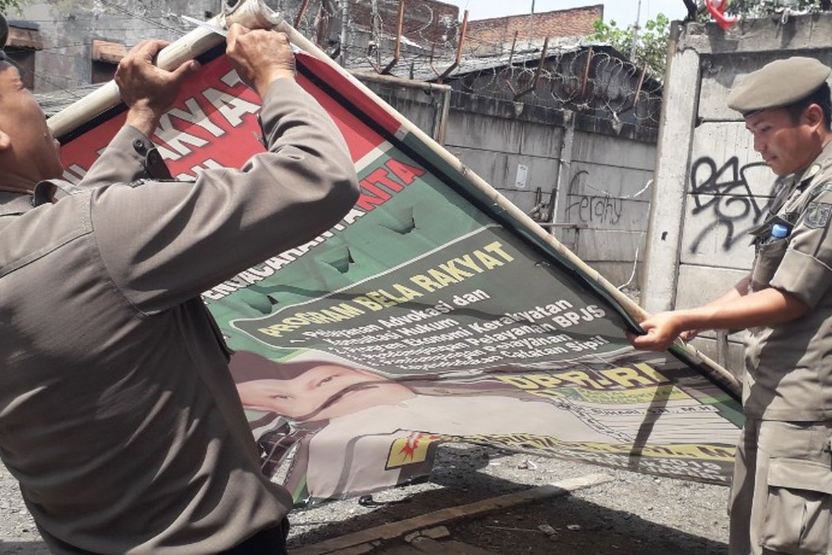 Petugas Satpol PP dan Bawaslu Jakarta Utara mencopot salah satu spanduk kampanye yang terpasang di Jalan Yos Sudarso, Jakarta Utara, Rabu (13/3/2019).