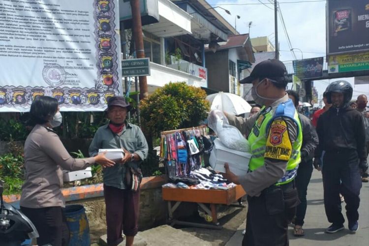 Anggota polisi di Kabupaten Cianjur, Jawa Barat membagikan nasi boks kepada warga di kawasan Puncak, Minggu (19/4/2020) dalam upaya meringankan beban masyarakat kurang mampu yang terdampak pandemi corona.