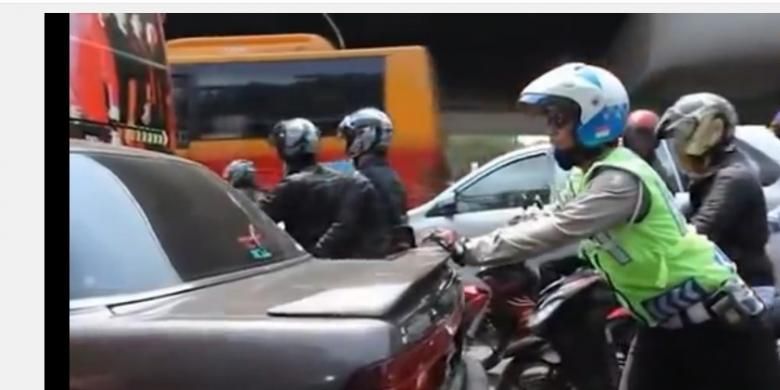 Seorang polisi tengah mendorong mobil mogok di tengah kemacetan di kawasan Pancoran, Jakarta Selatan.