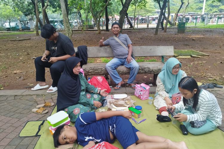 Herman (49) dan keluarganya piknik di kawasan Monas, Jakarta Pusat, Kamis (11/4/2024)