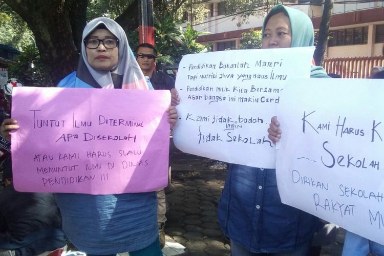 tampak orang tua tengah membawa kertas karton bertuliskan protes terkait PPDB jalur non akademis di depan kantor Disdik Jabar. 