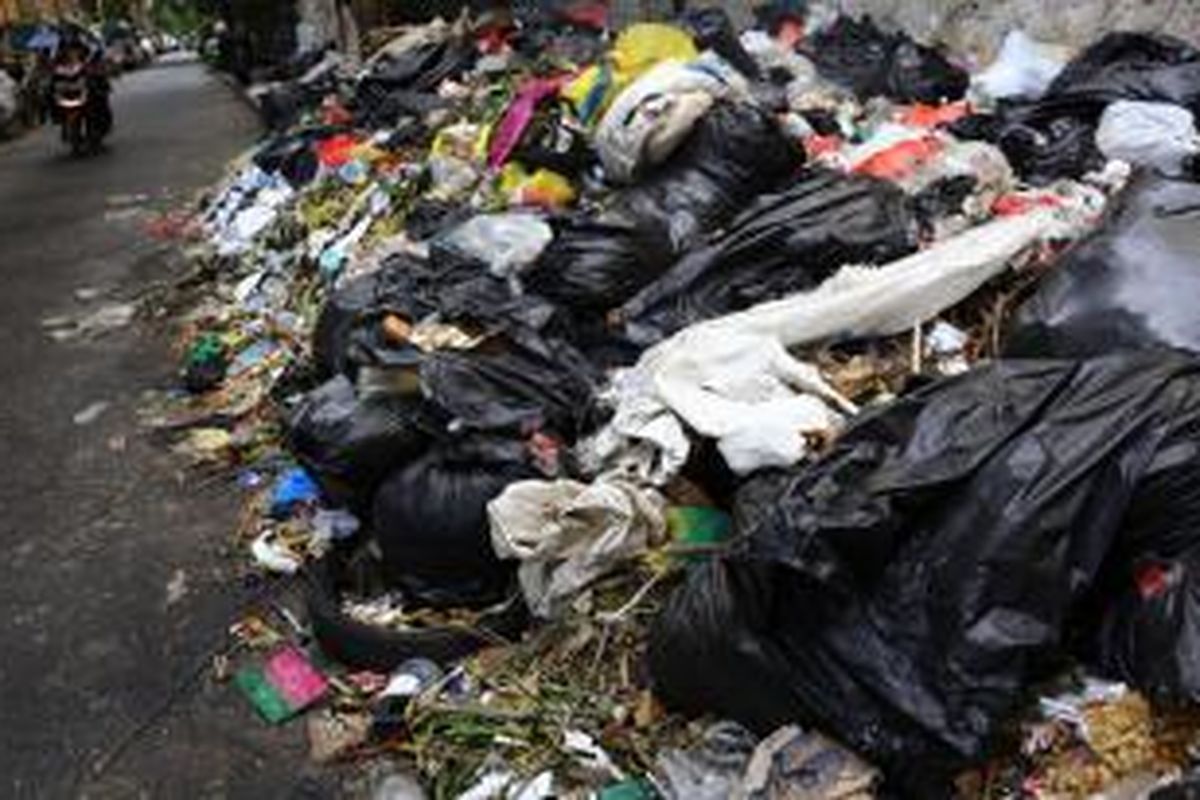 Pengendara melintas di samping sampah yang menumpuk di kawasan Cikini, Jakarta Pusat, Jumat (9/1/2015). Sampah menumpuk lantaran sudah beberapa hari tidak diangkut hingga menimbulkan bau tidak sedap.