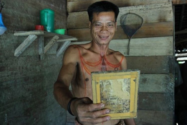 Seorang pria di Desa Simatalu melihat tato barunya di depan cermin.
