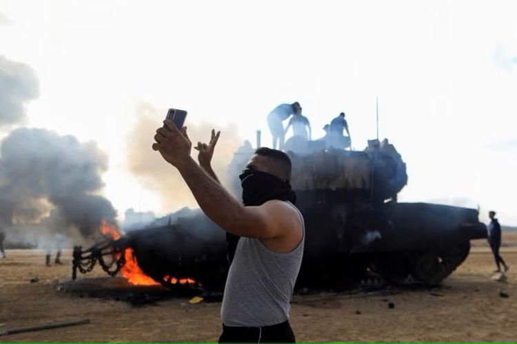 Seorang pria Palestina berswafoto di depan kendaraan militer Israel yang terbakar setelah ditembaki orang-orang bersenjata Palestina yang menyusup ke bagian wilayah perbatasan Israel-Gaza yang dikuasai oleh Israel, Sabtu, 7 Oktober 2023.