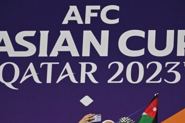 Dua orang suporter berfoto di depan logo Piala Asia 2023 yang terpajang di luar Stadion Al Janoub, Al Wakrah, pada Senin (15/1/2024). Jadwal Piala Asia 2023 hari ini akan menyajikan laga-laga yang berpengaruh ke nasib timnas Indonesia. (Foto oleh HECTOR RETAMAL / AFP)