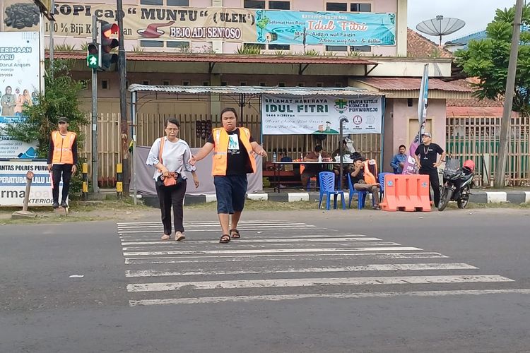 Pemuda katolik sedang menyeberangkan pengguna jalan di depan Pos Mudik 