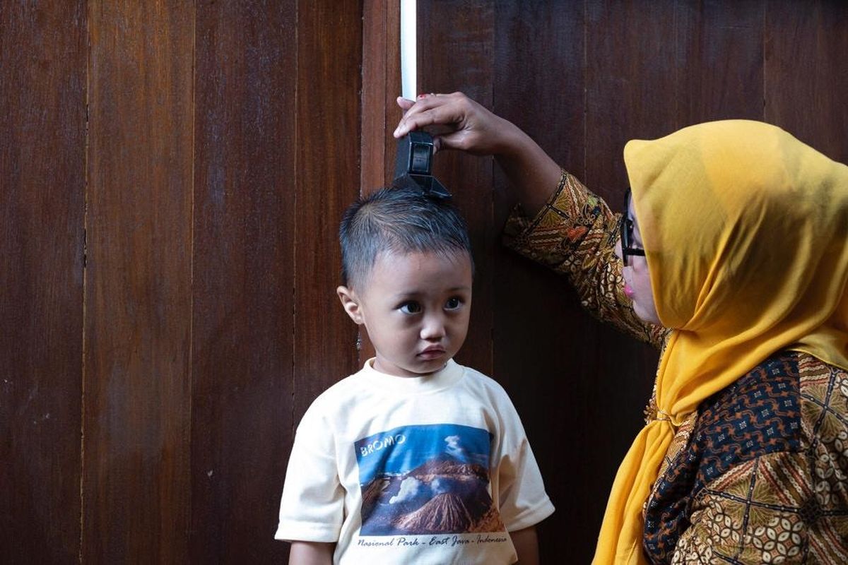 Petugas kesehatan sedang mengukur tinggi badan seorang anak