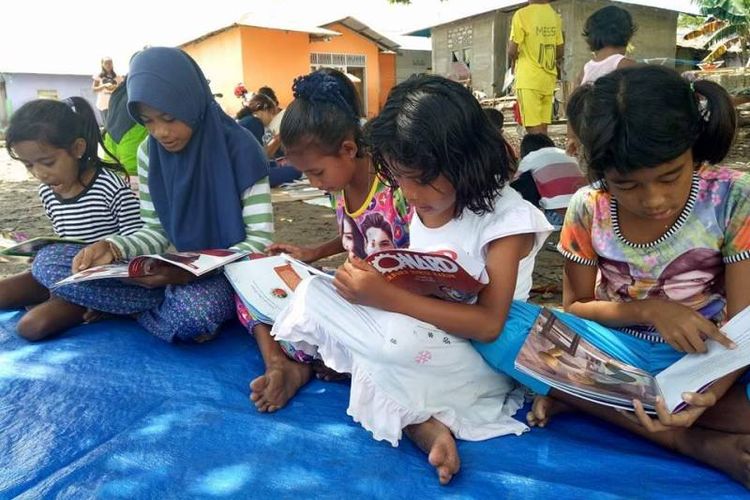 Beberapa orang anak tampak serius membaca buku kesukaannya saat Rumah Baca Barakate, Komunitas Hikayat Tanah Hitu, membuka lapak baca di sebuah tanah lapang di Desa Hitu Mesing, Kecamatan Leihitu, Kabupaten Maluku Tengah, Minggu, (30/5/2017).