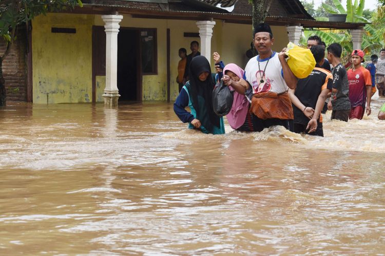 Warga melintasi jalan yang terendam banjir di Desa Kedungrejo, Pilangkenceng, Kabupaten Madiun,  Jawa Timur, Rabu (6/3/2019). Sejumlah anak Sungai Madiun meluap dan merendam sejumlah desa di wilayah tersebut, sehingga ratusan warga yang terjebak banjir harus dievakuasi ke tempat yang lebih aman.
