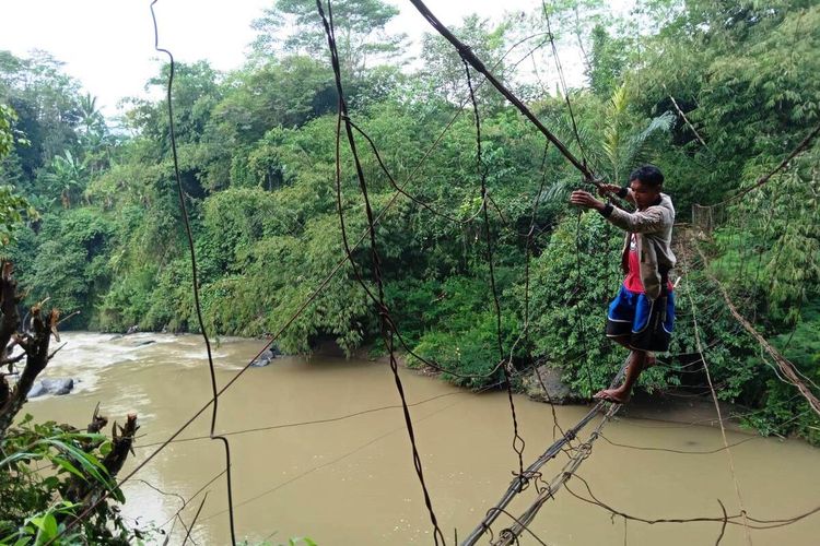 Seorang warga di Kabupaten Cianjur, Jawa Barat, ini bertaruh nyawa menyebrangi aliran sngai Cikondang, Kecamatan Cibeber dengan meniti seutas tali sling sambil berpegangan pada kawat di atas jembatan gantung yang sudah rusak, Rabu (22/6/2022).