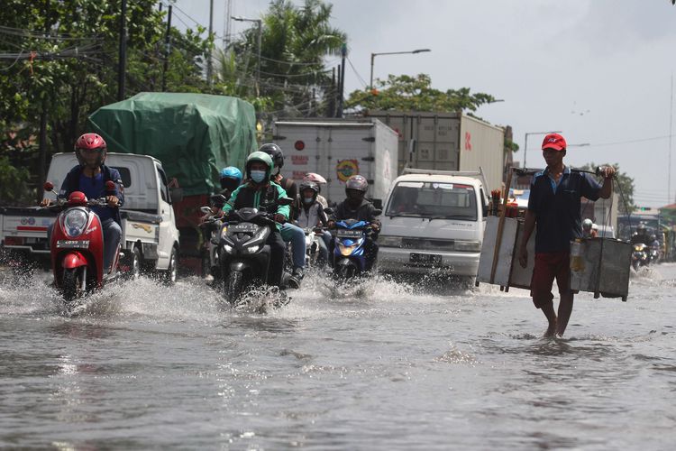 Sejumlah pengendara kendaraan bermotor melintasi banjir rob di Jalan Kalianak, Surabaya, Jawa Timur,  Kamis (19/5/2022). Pasang air laut yang tinggi menyebabkan jalan tersebut tergenang banjir rob dan mengakibatkan kemacetan panjang.