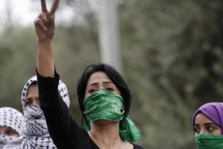 Perempuan Palestina, dengan menutup mulut menggunakan syah Hamas, emngacungkan tanda victory saat bentrokan dengan tentara Israel di Beit El, dekat ramalla, Tepi Barat, 10 Oktober 2015.
