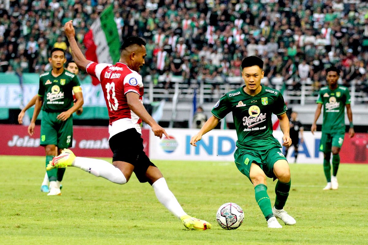 Pemain Madura United menghalau tendangan pemain Persebaya Surabaya Sho Yamamoto saat pertandingan pekan 4 Liga 1 2022-2023 yang berakhir dengan skor 2-2 di Stadion Gelora Bung Tomo Surabaya, Minggu (14/8/2022) sore. Link live streaming laga Madura United vs Persebaya dapat diakses di akhir artikel ini.