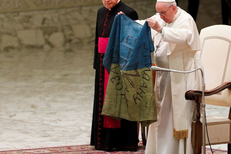 Paus Fransiskus memegang bendera Ukraina yang dikirimkan kepadanya dari kota Bucha di mana tubuh terikat ditembak dari jarak dekat, kuburan massal dan tanda-tanda eksekusi lainnya ditemukan, selama audiensi umum mingguan di Aula Paulus VI di Vatikan,  6 April 2022.