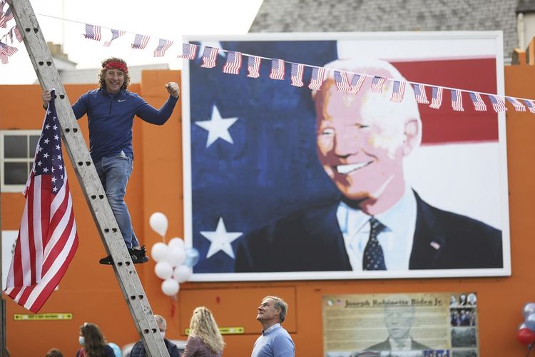 Seorang pria mengibarkan bendera AS di kota Ballina, rumah leluhur Presiden AS terpilih Joe Biden, di Barat Laut Irlandia, Sabtu (7/11/2020). Biden mengalahkan Presiden Donald Trump dalam pilpres AS 2020.