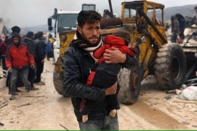 Seorang pria membawa korban di desa Besnia dekat perbatasan Turkiye di Suriah.
