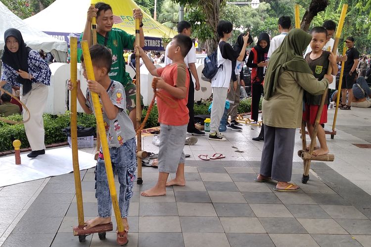 Anak-anak pengunjung Car Free Day (CFD) Taman Bungkul, Surabaya saat mencoba permainan egrang di stan Kampoeng Dolanan, Minggu (23/2/2025).