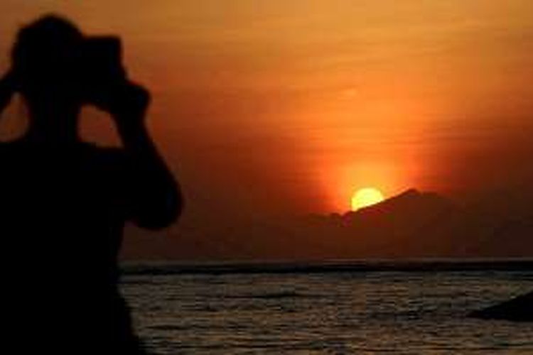 Wisatawan mengabadikan pesona matahari terbit dari balik Gunung Rinjani di Pulau Lombok yang terlihat dari Pantai Karang Sanur, Denpasar, Bali, Selasa (16/8/2016).