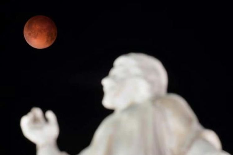 Gerhana bulan terlihat dengan latar depan Monumen El Salvador del Mundo di San Salvador, El Salvador, 15 April 2014. Gerhana bulan kali ini terbilang langka karena bulan berubah warna dari oranye ke merah darah.