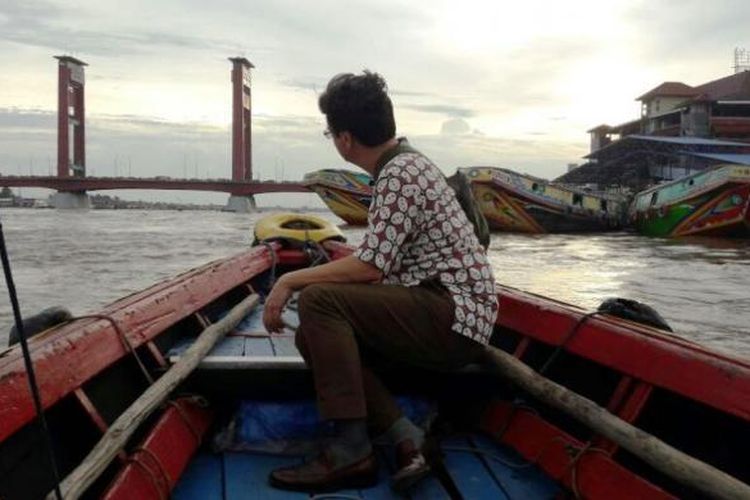 Karim Raslan menaiki getek melintasi Sungai Musi. Getek adalah perahu mesin sepanjang enam meter yang berbentuk ramping dan terbuat dari kayu, yang berfungsi sebagai transportasi air untuk menyebrangi Sungai Musi.