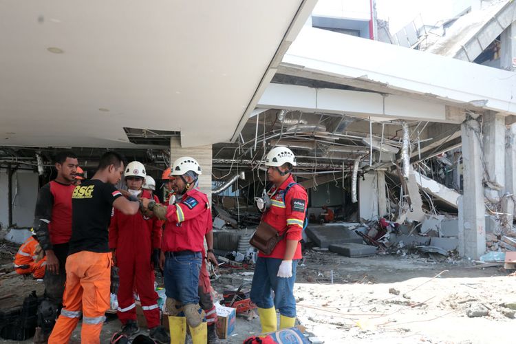 Sejumlah anggota Basarnas sedang mendiskusikan cara mengeluarkan seorang jenazah di reruntuhan Hotel Mercure, Palu. Posisi jenazah tertimpa 3 beton di sebuah ruangan.