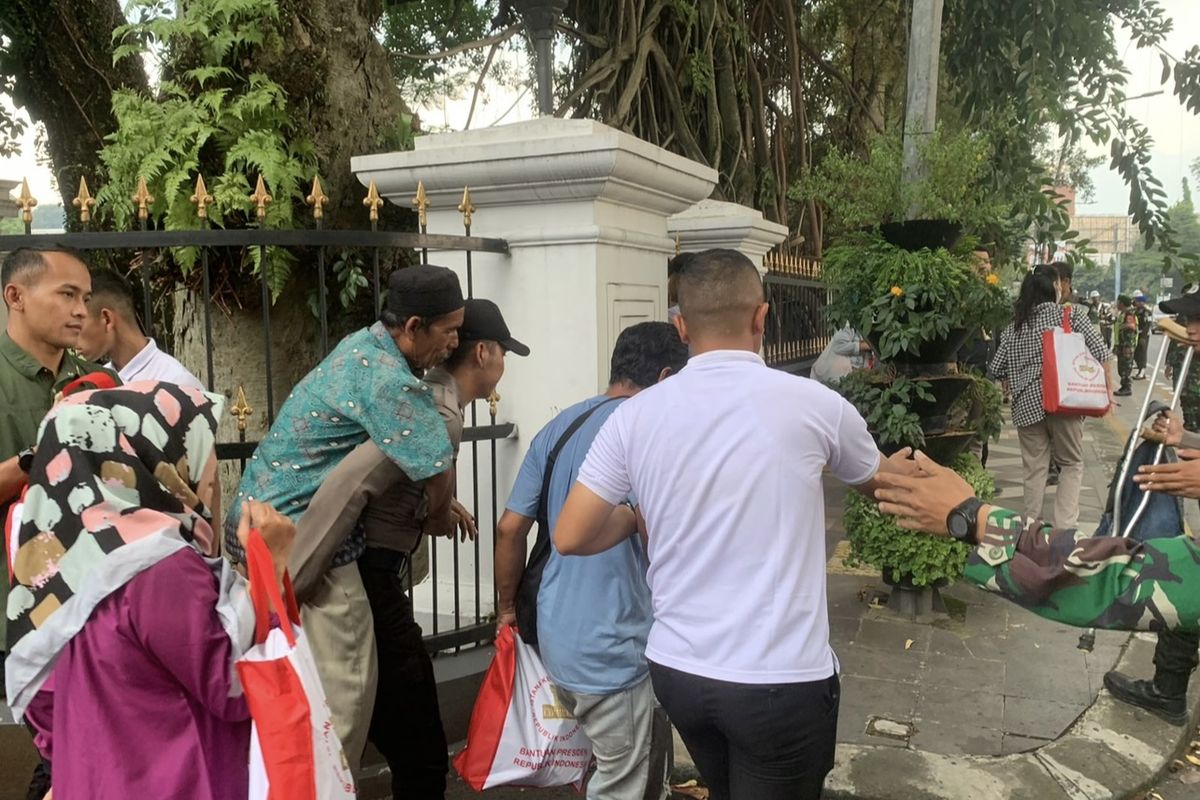 Momen pria paruh baya digendong Polisi saat sedang mengantre paket sembako dari Presiden Joko Widodo di kompleks sekitaran Istana Bogor, Minggu (7/4/2024).