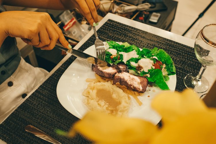 Ilustrasi memotong daging saat makan di restoran. 