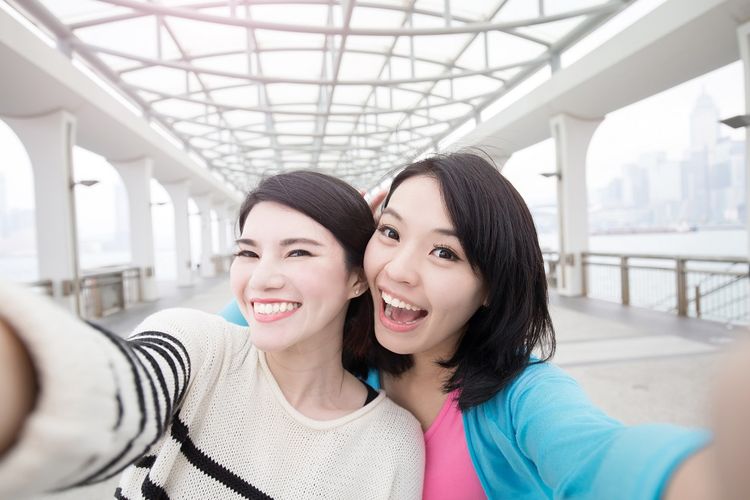 Ilustrasi dua orang wanita melakukan group selfie menggunakan kamera depan ponsel