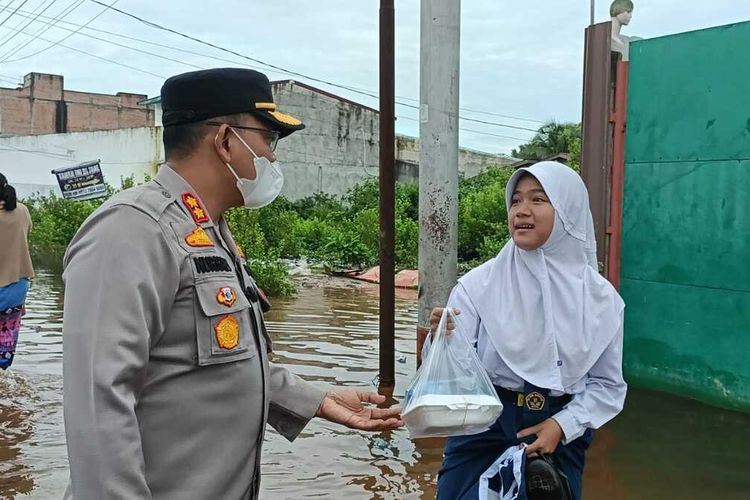 Petugas kepolisian memberikan bantuan paket makanan kepada salah seorang anak sekolah yang melewati genangan banjir rob di Kota Dumai, Riau, Jumat (25/11/2022) pagi.