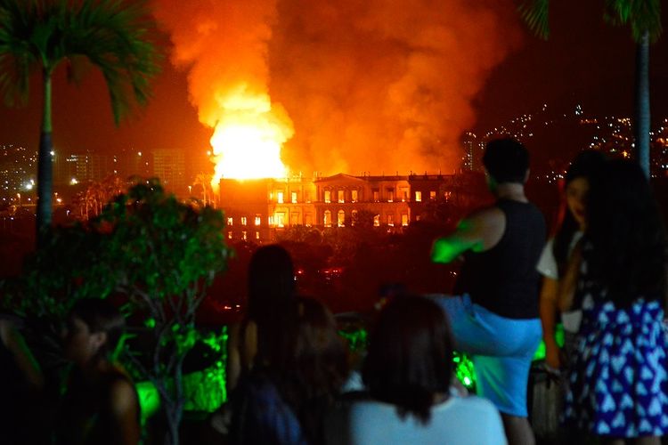 Warga menyaksikan api yang melalap gedung museum nasional Brasil di Rio de Janeiro, Minggu (2/9/2018). Bangunan ini merupakan institusi sains tertua di negeri itu.