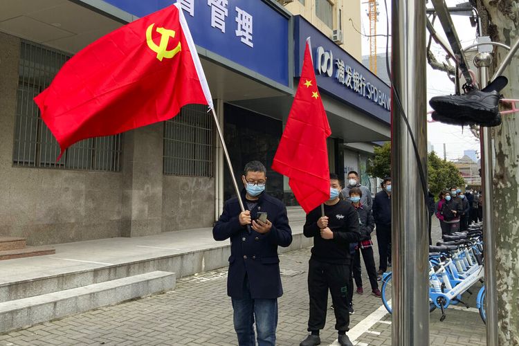 Warga membawa bendera Partai Komunis dan bendera nasional China ketika yang lain bersiap untuk mengambil bagian dalam tes COVID massal putaran pertama di distrik Jingan, Shanghai barat, China, Jumat, 1 April 2022.