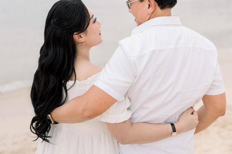 Puput Nastiti Devi tampil anggun dengan long dress putih, makeup natural, dan rambut wavy saat foto kehamilan anak ketiga bersama keluarga.