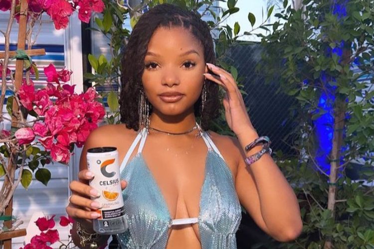 Halle Bailey mengenakan atasan berwarna aqua yang berkilau, celana pendek denims dan juga sepatu boots koboi.